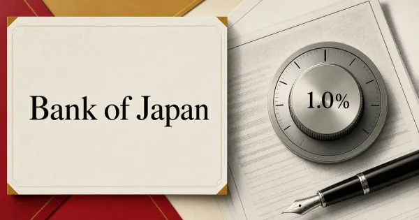 Large official Bank of Japan wordmark on an ivory policy-document plaque beside a grayscale 1.0% interest-rate dial, policy papers and a fountain pen.