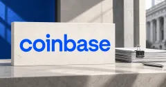 One large official blue lowercase coinbase wordmark on an off-white stone sign beside unbranded greyscale contract papers with a binder clip and pen, against blue and grey architectural panels.