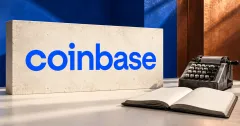 Large official blue Coinbase wordmark on an ivory stone sign beside an unbranded greyscale mechanical calculator and open blank ledger, against cobalt and copper panels.