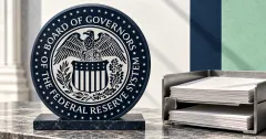 Large official monochrome Federal Reserve Board seal on a navy circular plaque beside stacks of unbranded greyscale reserve documents in a metal filing tray.