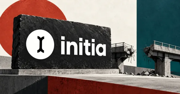 One large official white Initia icon and lowercase wordmark on a charcoal stone sign beside an unbranded greyscale broken bridge, against off-white, rust-red and deep-petrol panels.