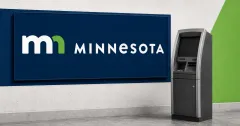 The official State of Minnesota wordmark on a large navy sign beside a greyscale, unbranded cryptocurrency kiosk with a blank dark screen.