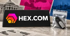 Large official HEX.COM gradient emblem and white wordmark on a charcoal desk sign beside an unbranded greyscale hardware wallet sealed in a clear evidence pouch, with magenta and blue panels and subdued Istanbul architecture.