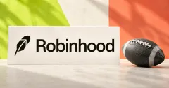 Large official black Robinhood feather and wordmark on an off-white desk sign beside one unbranded greyscale American football, against lime and coral panels.