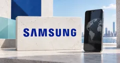 A large official blue SAMSUNG lettermark on an off-white stone sign beside an unbranded greyscale smartphone displaying a globe reflection, with blue and pale turquoise architectural panels and a distant skyline.