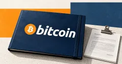 One large official orange Bitcoin emblem and white lowercase bitcoin wordmark on a navy investment folio beside unbranded greyscale financial paperwork with a metal clamp, on a pale stone desk against orange and slate-blue editorial panels.