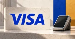 One large official blue VISA wordmark on an off-white limestone sign beside a smaller unbranded greyscale payment terminal with a blank screen, against cobalt-blue and ochre panels.