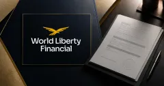 Large official gold World Liberty Financial logomark on a dark navy plaque beside a greyscale unbranded federal bank-charter approval document on an editorial desk.